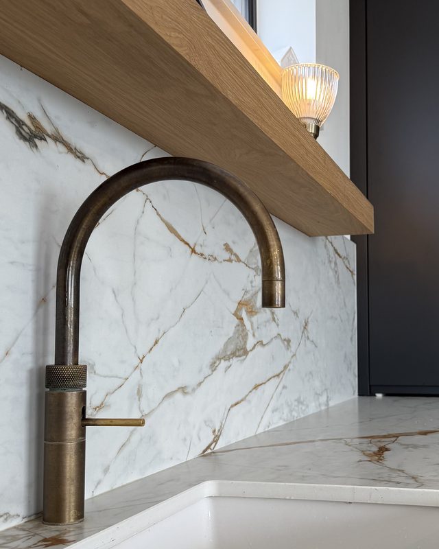 Brass tap against a veined marble splashback with a solid oak shelf